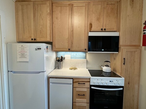 A compact kitchen with wooden cabinets, a white refrigerator, a microwave, a kettle, and a dishwasher. - The Whales are migrating! Watch from our deck! Walk to everything! (Yachats)