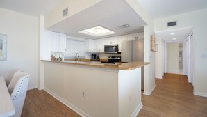 Una cocina moderna con armarios blancos, una isla central, electrodomésticos de acero inoxidable y suelo de madera.