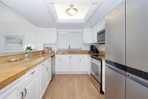 A modern kitchen with white cabinets, a stainless steel refrigerator, and a wooden countertop.
