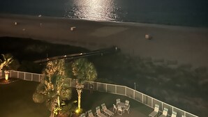 Vista da praia com a lua no céu, uma faixa de areia e cadeiras de praia à beira-mar.