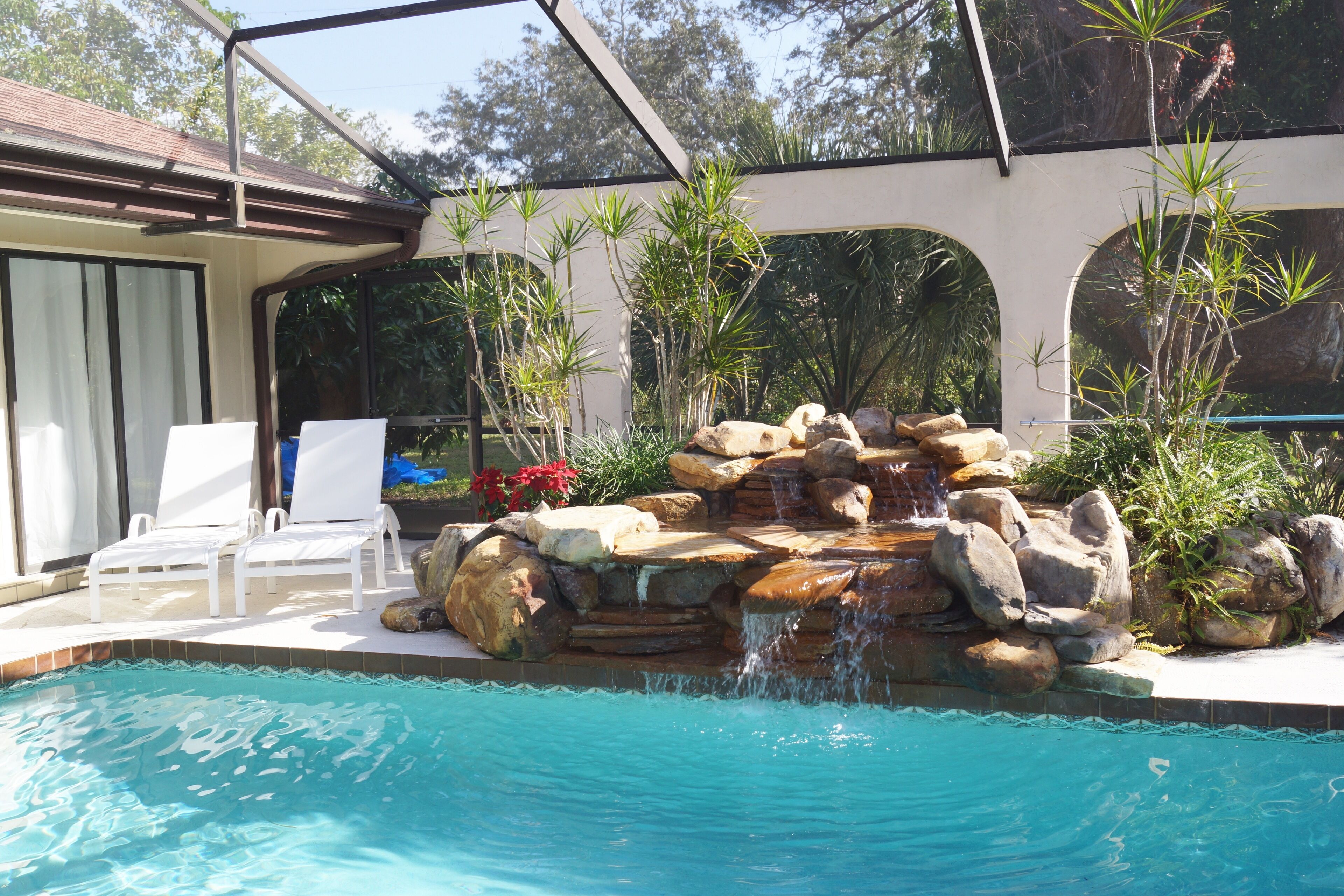A swimming pool with a waterfall feature, surrounded by rocks and plants.