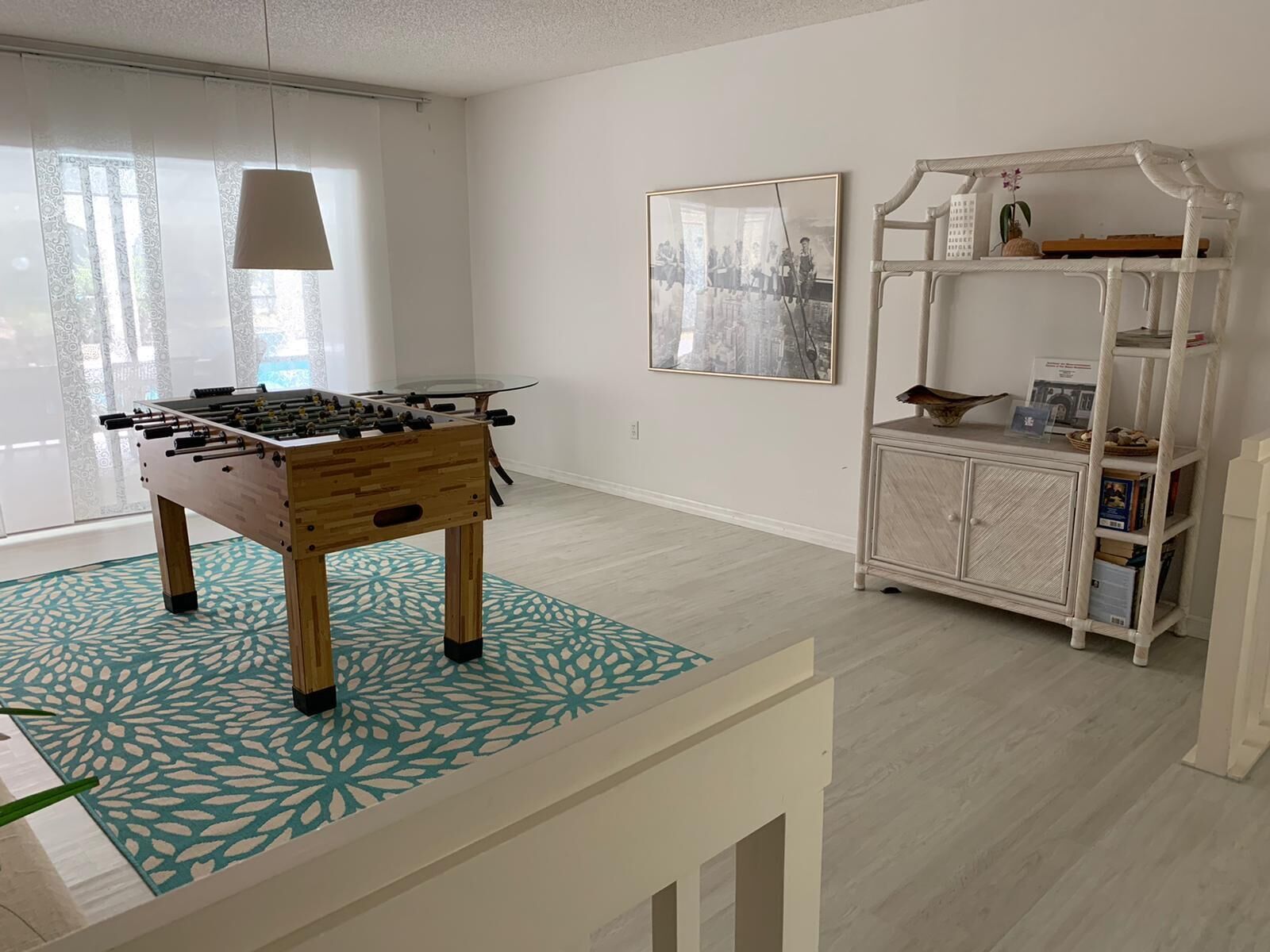 A room with a foosball table, a patterned rug, a cabinet with shelves, and a framed picture on the wall.