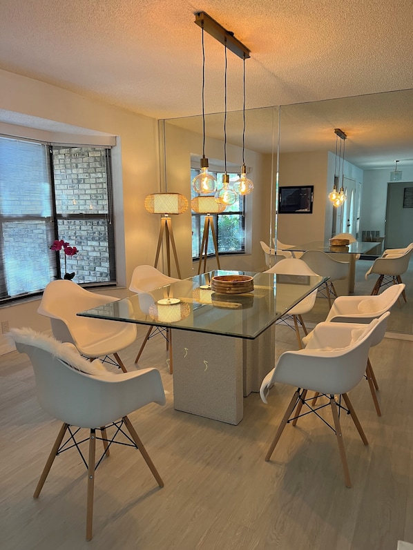 A modern dining area with a glass table, white chairs, and pendant lights.