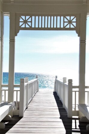 A wooden pier leading to a beach with a clear view of the ocean.
