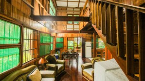 A spacious wooden interior with high ceilings, large windows, and a central dining area. - Cozy Caribbean Beachfront House (Pet & Kid Friendly) (Puerto Viejo)