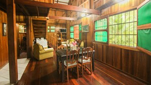 A wooden interior with a dining area, sofa, and large windows. - Cozy Caribbean Beachfront House (Pet & Kid Friendly) (Puerto Viejo)