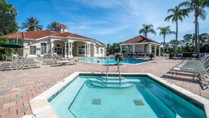 Uma área de piscina com espreguiçadeiras, um edifício com telhado de telhas vermelhas e palmeiras.