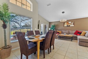 Un espacio habitable amplio con una mesa de comedor, sillas, un sofá y una mesa de centro. Hay un ventanal grande que proporciona luz natural y vistas al exterior.