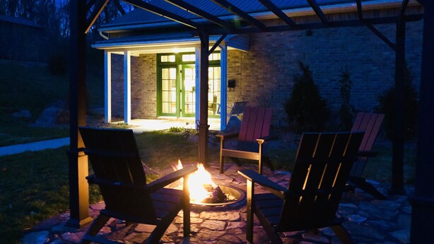 A covered outdoor seating area with a fire pit, chairs, and a building entrance with glass doors. - STONES THROW RETREAT in Downtown Lewisburg (Lewisburg)