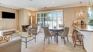 En moderne stue med sofalounge, glasbord og pejs. Spiseområde med rundt bord og stole. Store vinduer og udsigt til naturen.