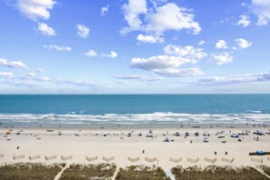 A beach with umbrellas and beachgoers, a clear sky, and the ocean.