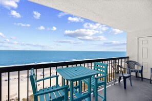 Een balkon met uitzicht op het strand en de oceaan, met een tafel en stoelen.