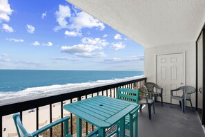 A balcony with a view of the ocean, a table, and two chairs.
