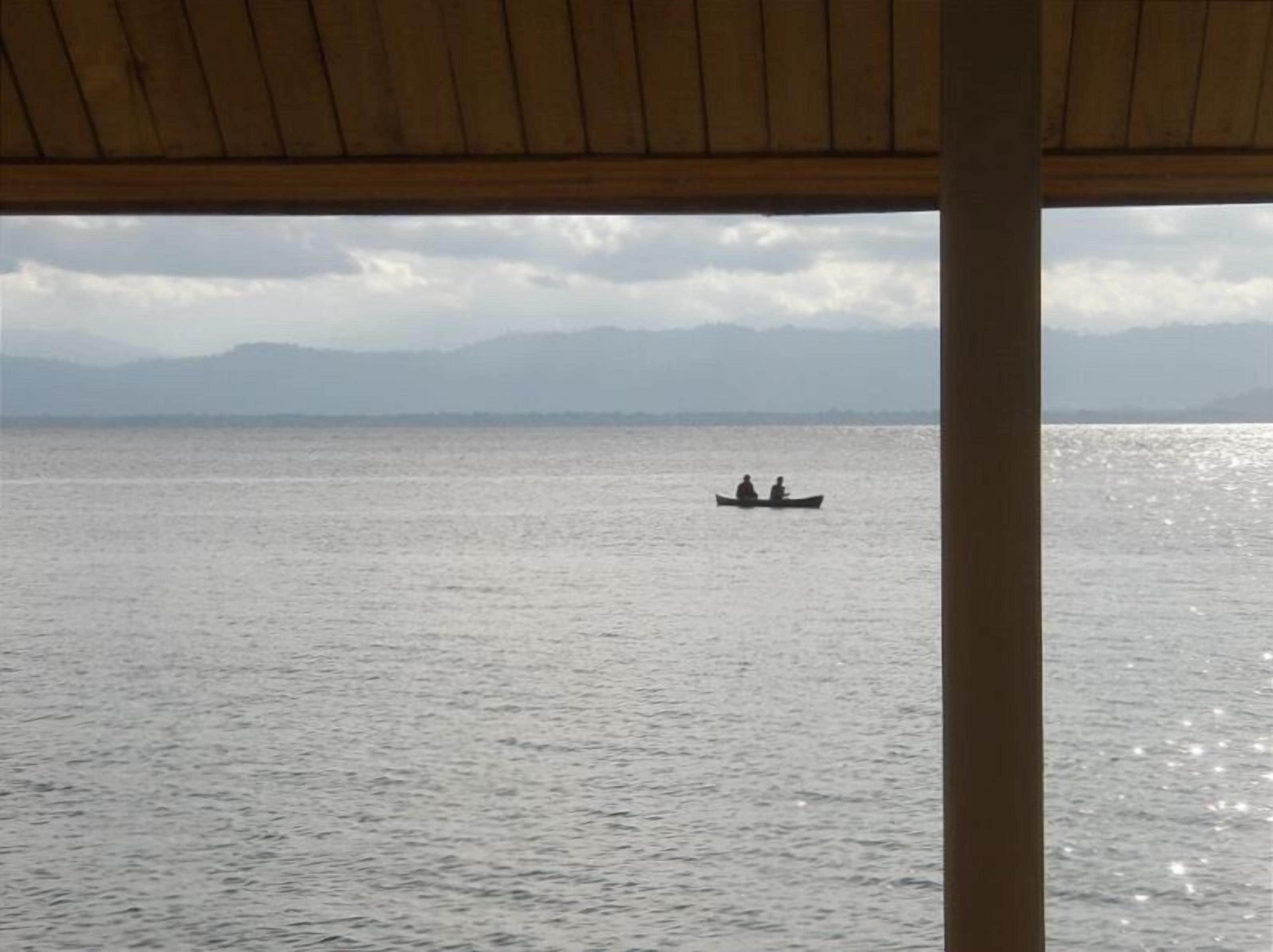 Vista de un lago tranquilo con montañas al fondo y una estructura de madera en primer plano.