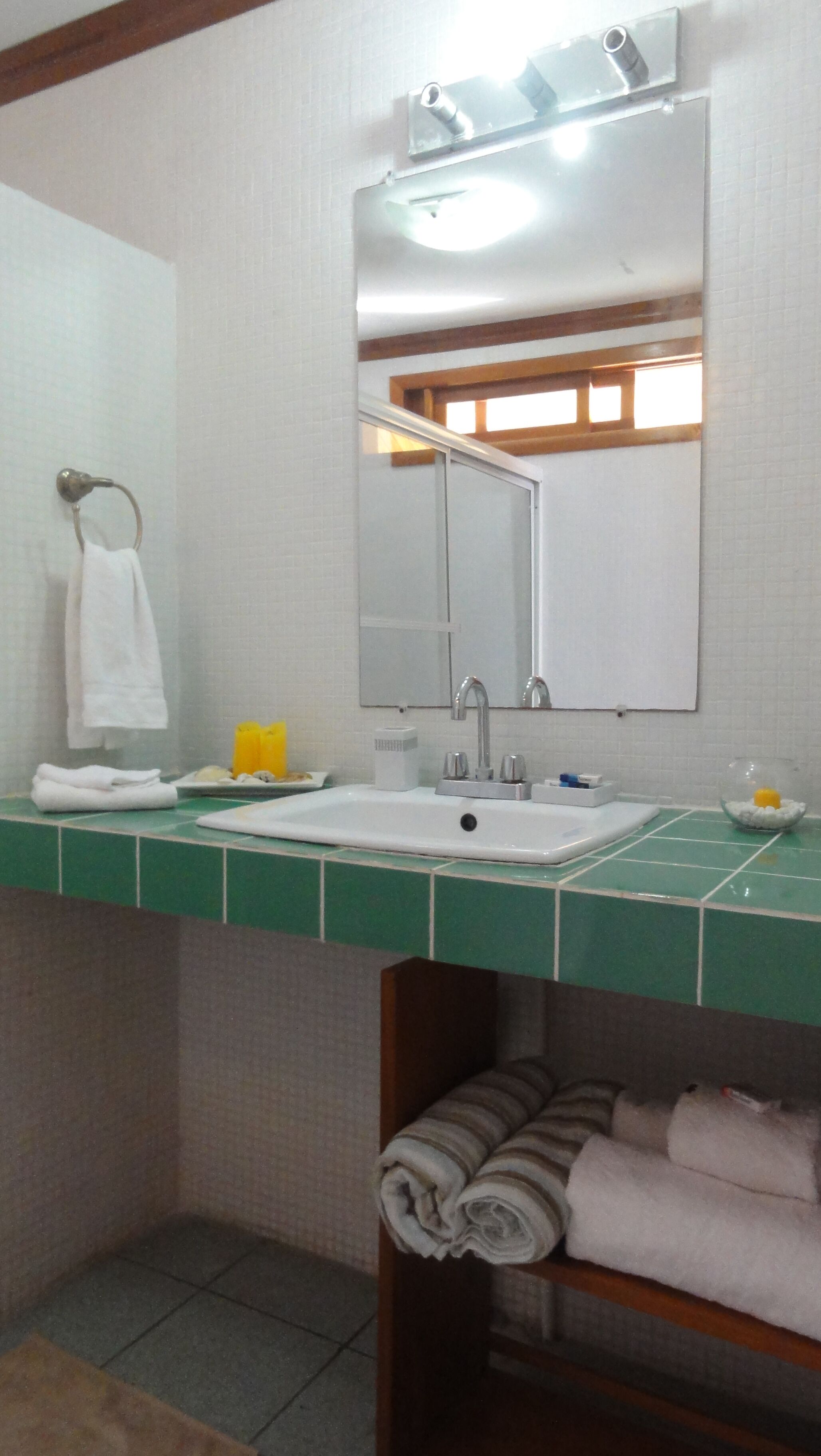 A bathroom with a white sink, mirror, and green tiled countertop. There is a towel rack with a white towel and a yellow soap dispenser.