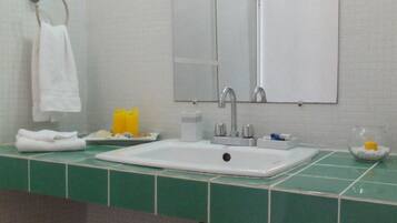 A bathroom with a white sink, mirror, and green tiled countertop. There is a towel rack with a white towel and a yellow soap dispenser.