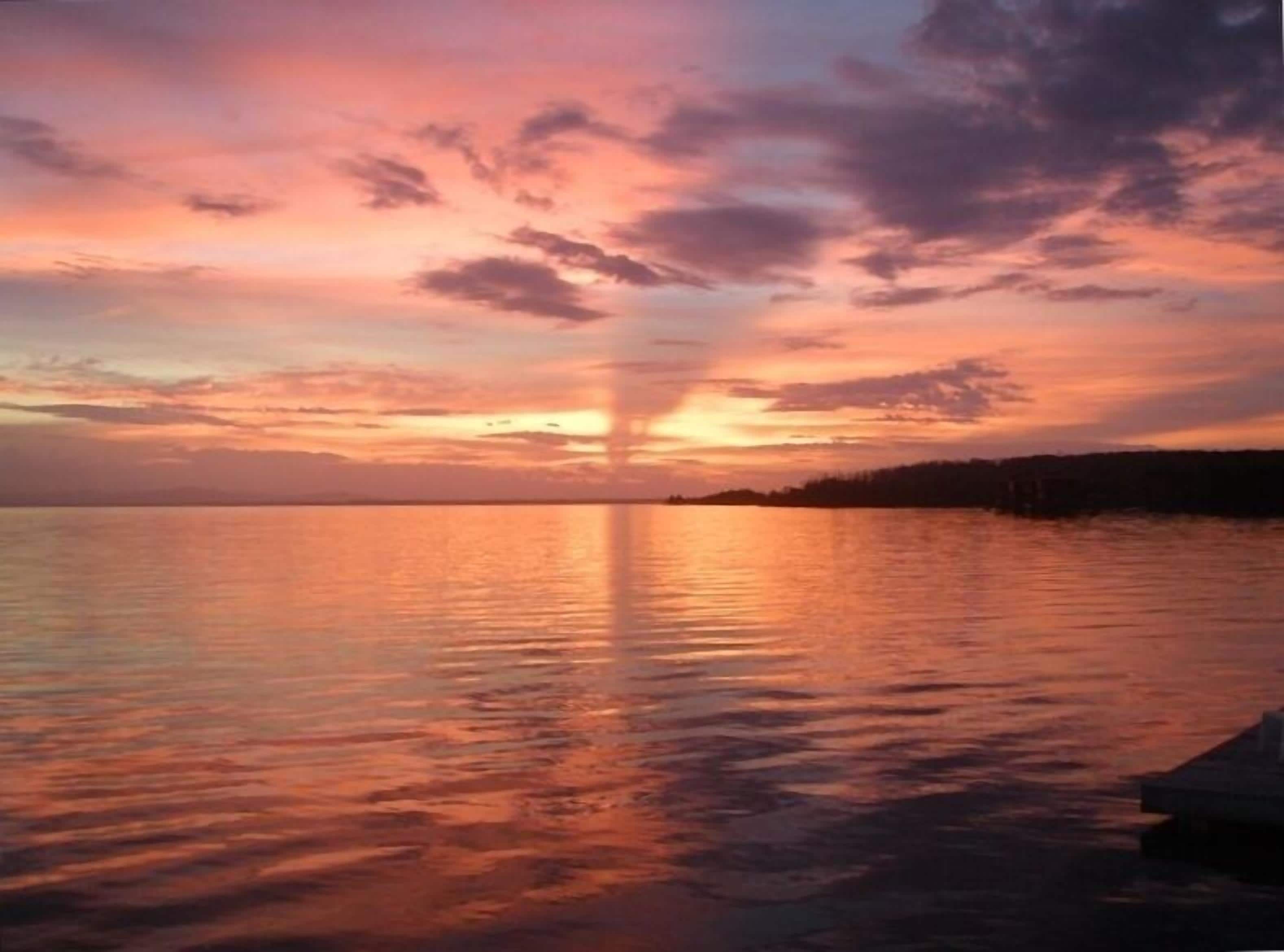 Atardecer sobre una masa de agua tranquila, con la silueta de una tierra en la distancia.