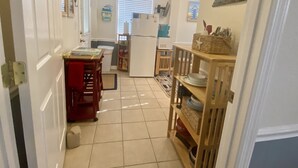 Een smalle keuken met witte kastjes, een koelkast en een houten eettafel met stoelen.