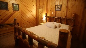 Una stanza in una baita di legno, con un letto, un comodino e quadri appesi alle pareti.