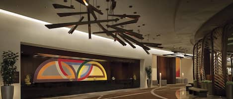 A modern lobby with a curved reception desk, abstract wall art, and a unique ceiling design.