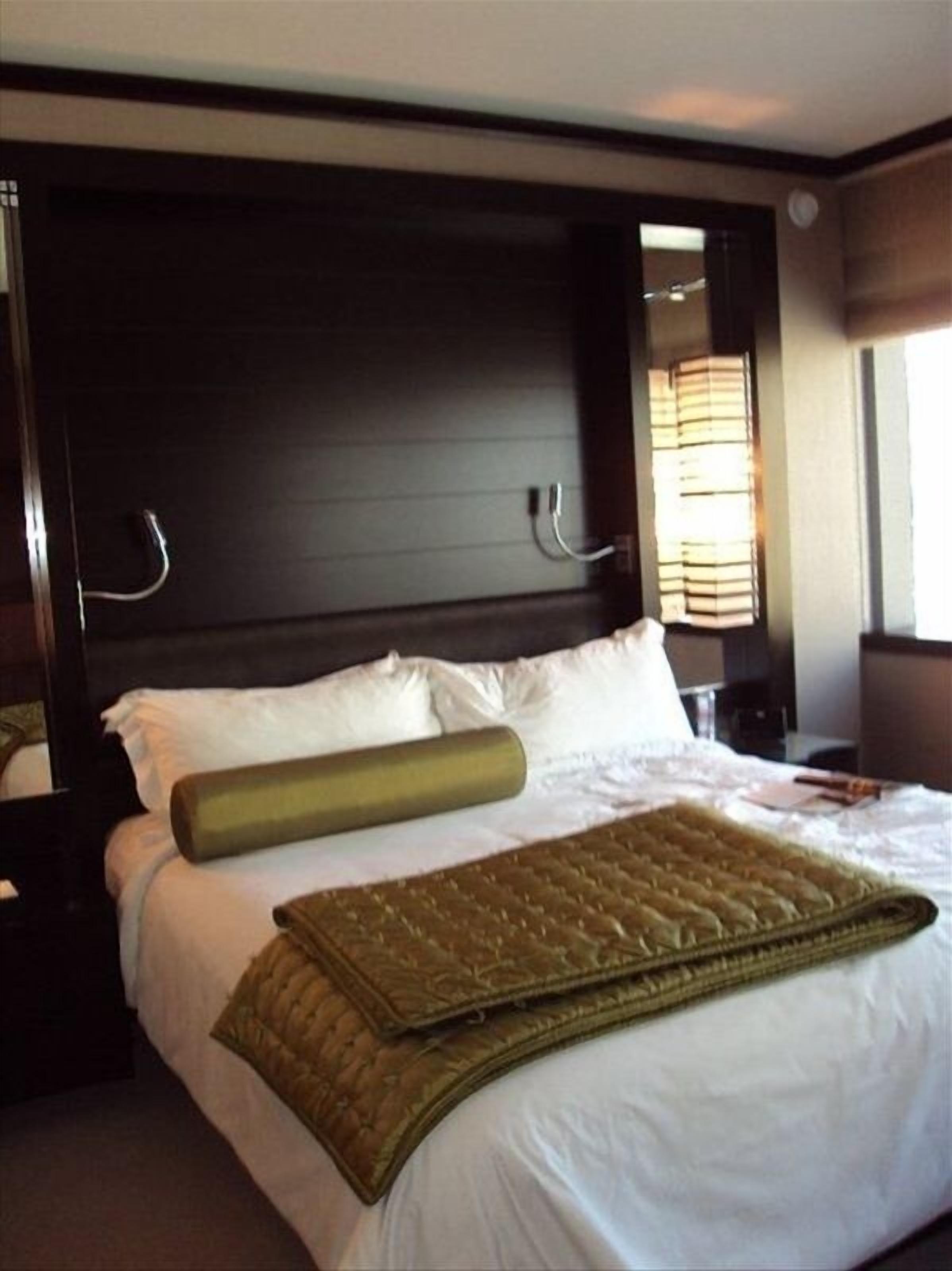 A hotel room with a large bed, dark headboard, and a window with blinds.