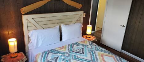 A bed with a wooden headboard, white pillows, a colorful patterned bedspread, and two bedside lamps on wooden nightstands.