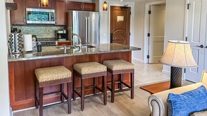 Una cocina moderna con electrodomésticos de acero inoxidable, encimera de mármol y taburetes de bar de madera.