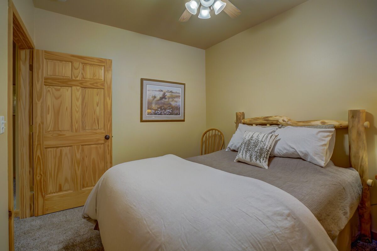 A bedroom with a wooden door, a bed with white bedding, a headboard made of wood, and a ceiling fan.