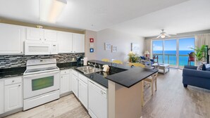 Una cocina moderna con armarios blancos, encimera negra y vistas al océano desde el balcón.