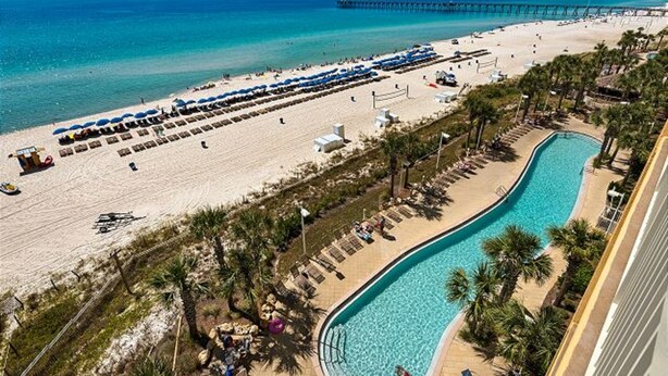 Un resort frente a la playa con piscina, sombrillas y un muelle al fondo.