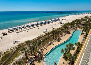 A beach resort with a swimming pool, beach umbrellas, and a pier in the background.