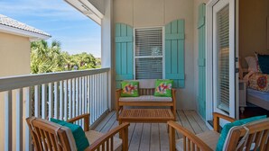 A wooden deck with a bench and chairs, a sliding glass door, and a view of palm trees. - Great beach house with access to pools and restaurants.
 (Miramar Beach)