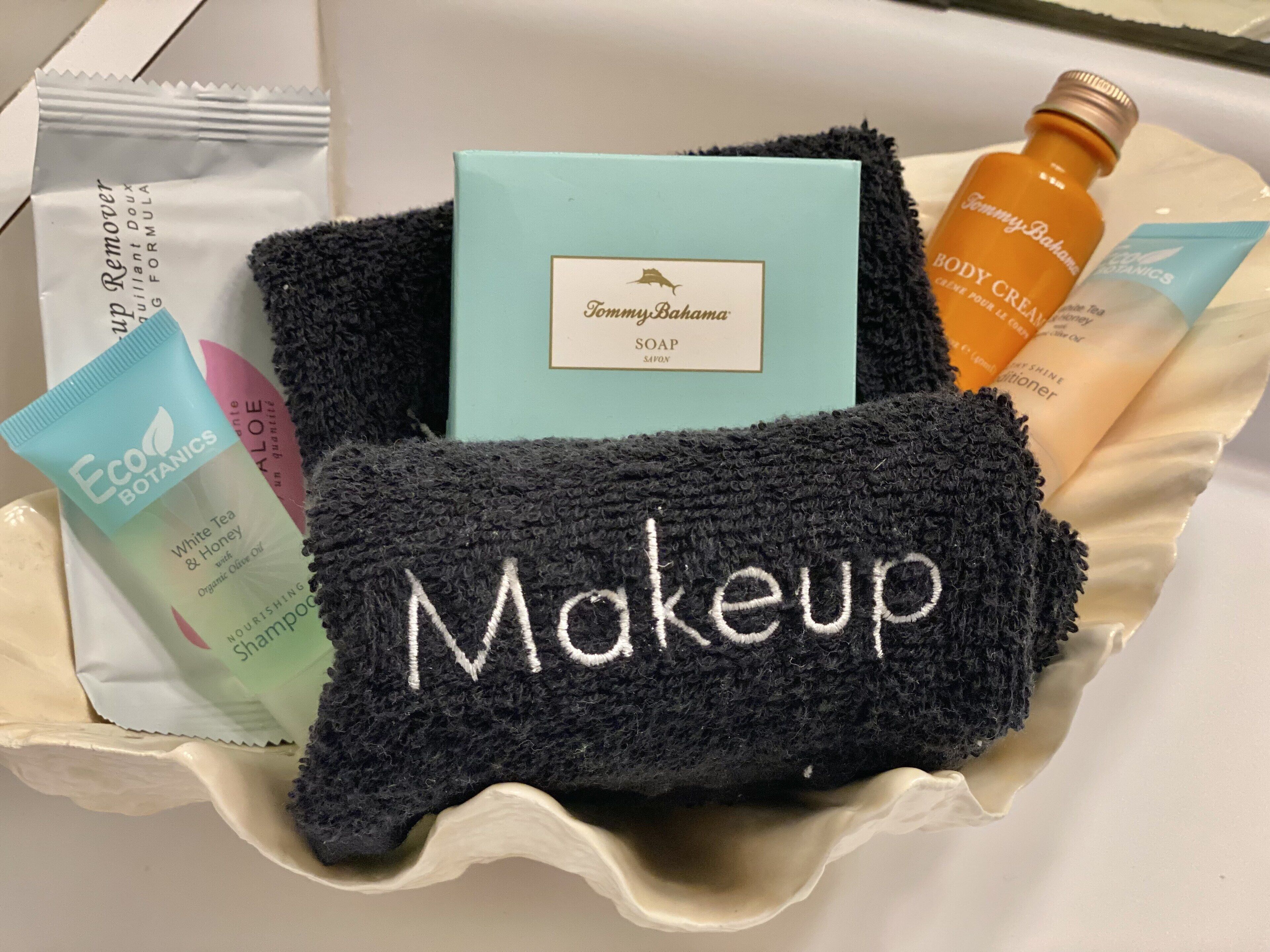 En presentkorg som innehåller olika produkter för personlig hygien, bland annat en flaska kroppskräm, en tvål och en svart handduk med broderad texten "Makeup".