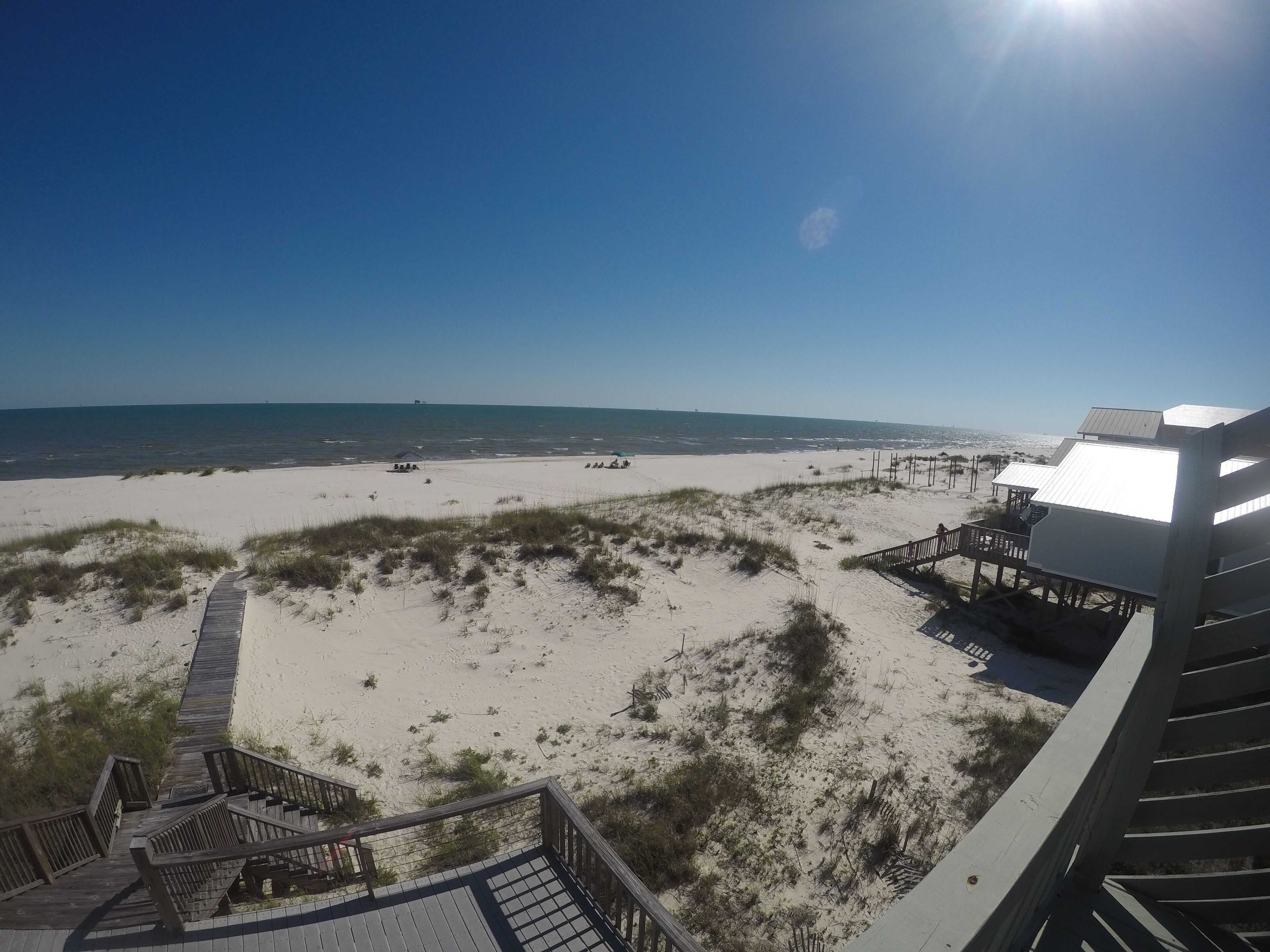 A beach view with a wooden boardwalk leading to a beach house with a deck.