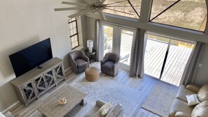 A spacious living room with a large TV, comfortable seating, a ceiling fan, and a view of the outdoors through large windows. - Relax With Walls Of Windows Directly On The Gulf! (Gulf Shores)