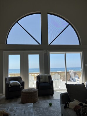 Quarto espaçoso com grandes janelas com vista para uma praia, mobiliado com duas poltronas, um sofá e uma mesa pequena.