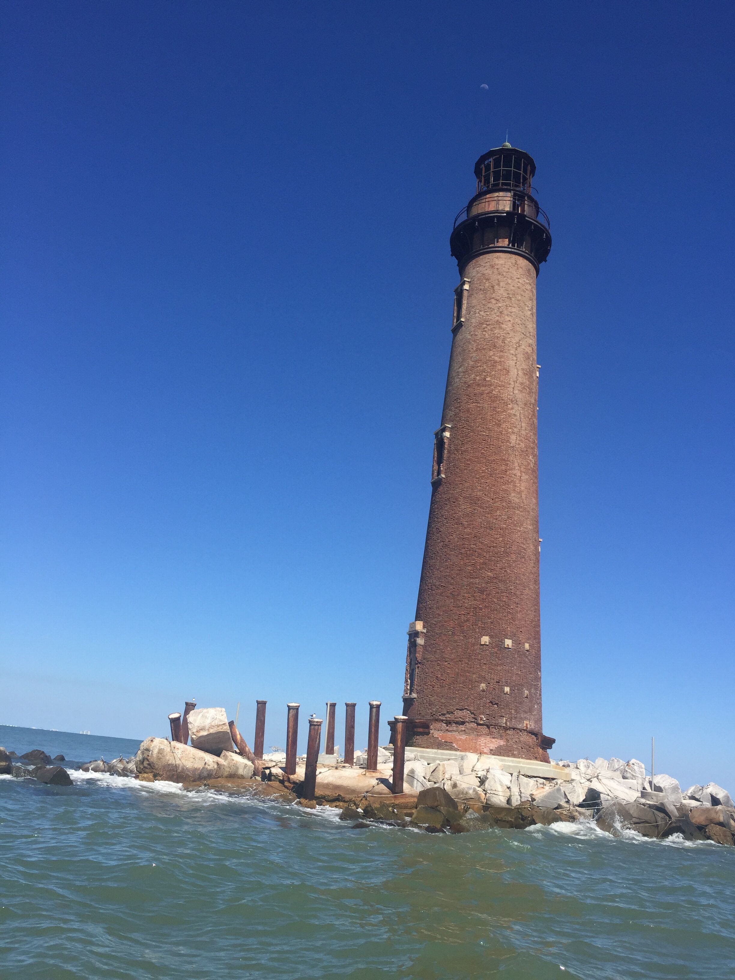 A tall, cylindrical brick lighthouse with a black top, situated on a rocky outcrop by the sea.