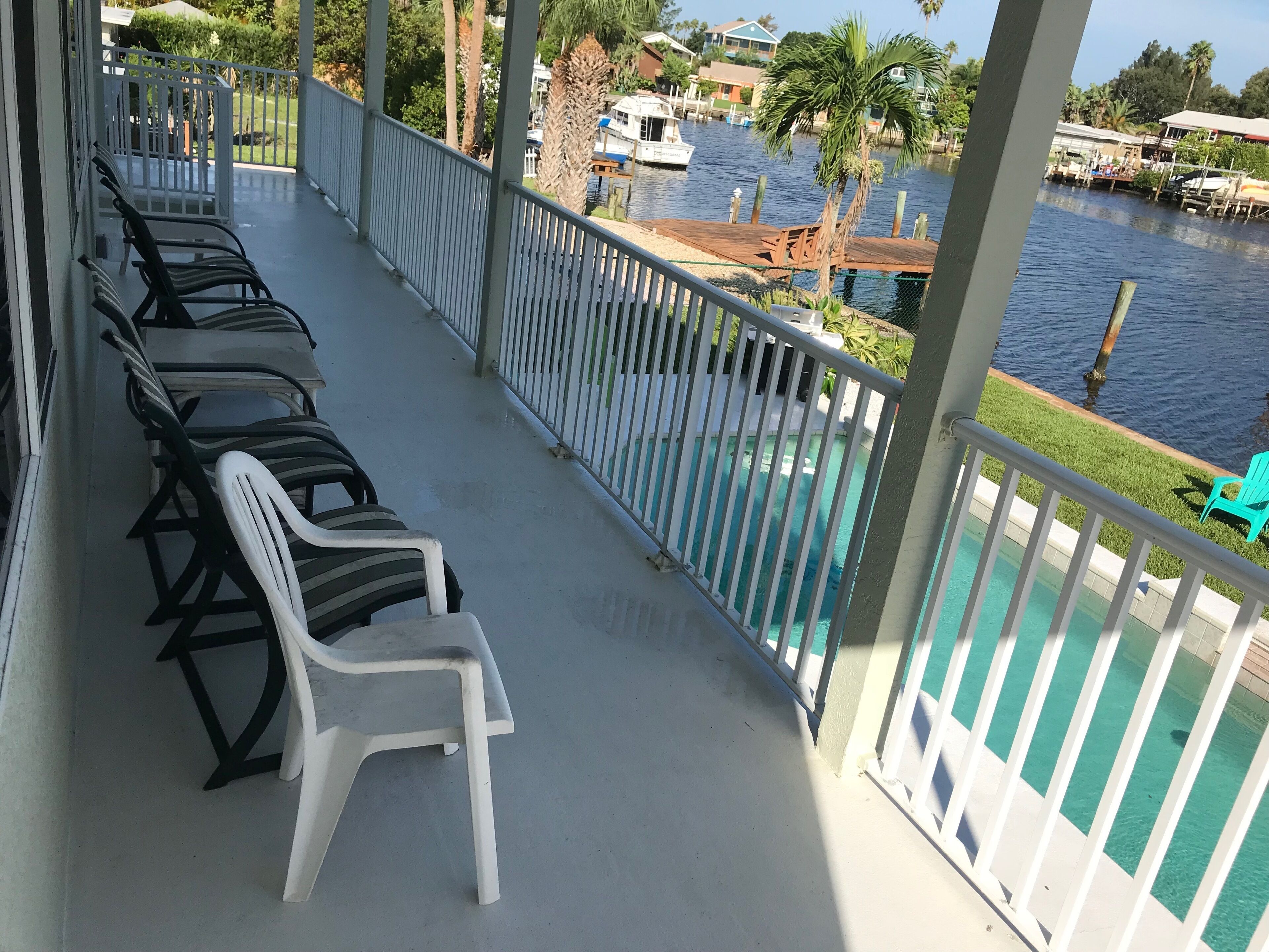 A balcony with a pool view, featuring a row of chairs and a small table.