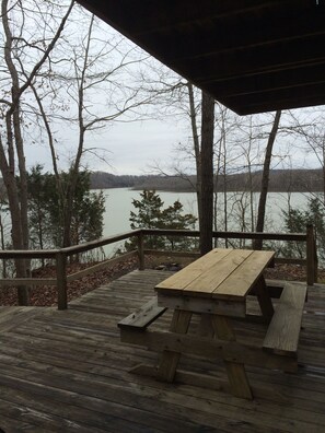 A wooden deck with a picnic table and benches overlooking a lake, surrounded by trees.
