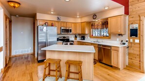 A modern kitchen with wooden cabinets, stainless steel appliances, and a central island with stools. - Hot Tub, Mtn Views & Seclusion - Moose Wetlands, 24mi Breck, Pets OK (Fairplay)