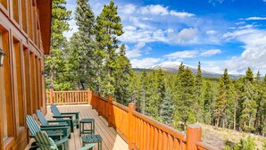 A wooden deck with green Adirondack chairs and a wooden railing overlooking a forested mountain area. - Hot Tub, Mtn Views & Seclusion - Moose Wetlands, 24mi Breck, Pets OK (Fairplay)
