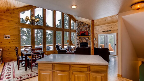 A cabin interior with a stone fireplace, wooden walls, large windows, and a dining area. - Hot Tub, Mtn Views & Seclusion - Moose Wetlands, 24mi Breck, Pets OK (Fairplay)