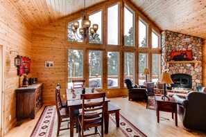 The beautiful great room has high vaulted ceilings and two-story windows. There is a large stone wood-burning fireplace.