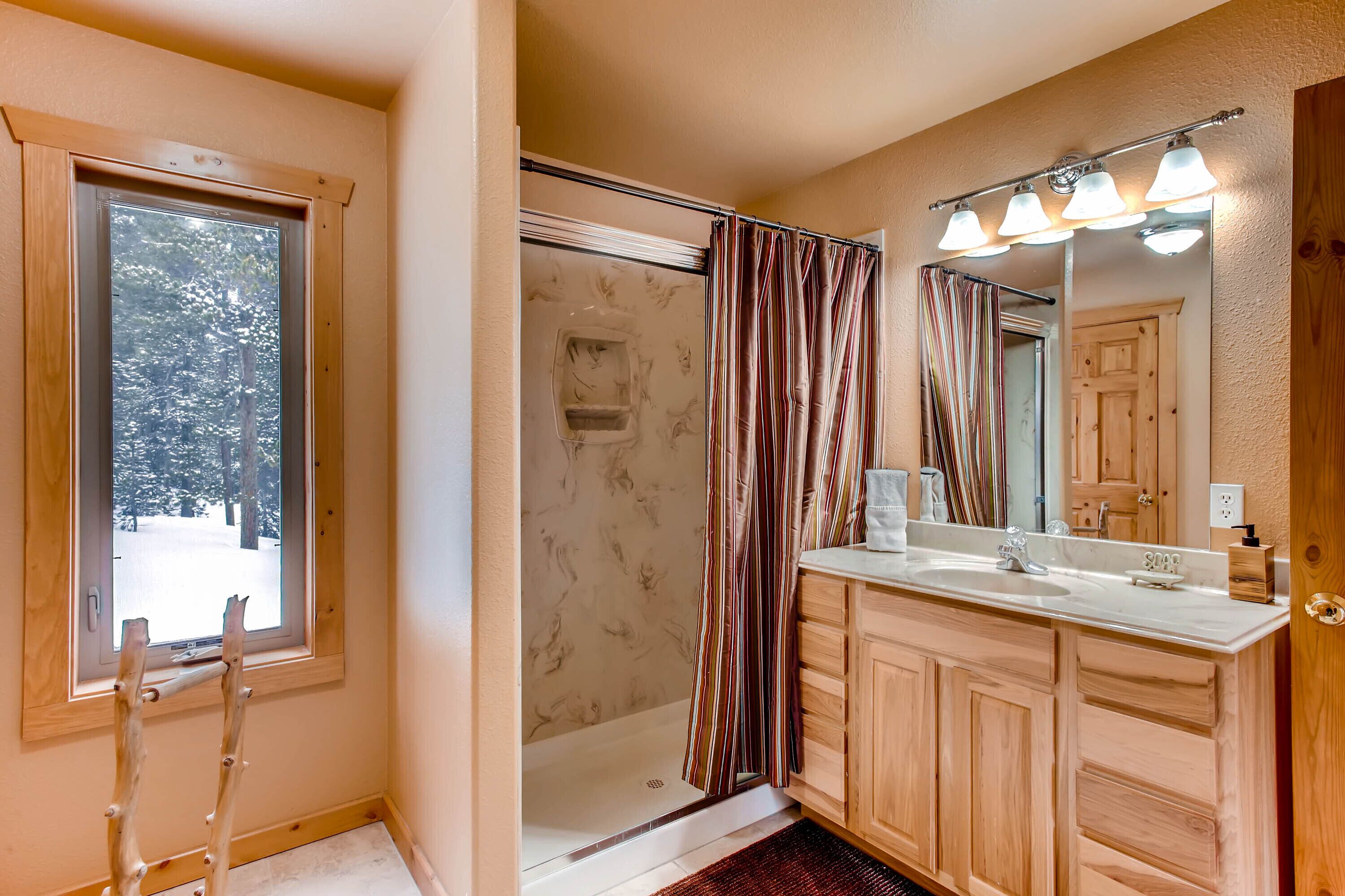 A bathroom with a shower, a vanity with a mirror, and a window.