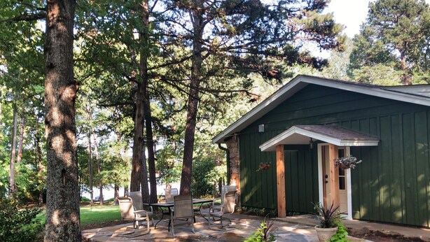 Una cabaña rústica con cimientos de piedra, rodeada de altos árboles y un patio de piedra.