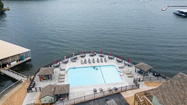 Ein Pool am Wasser mit Liegestühlen und Sonnenschirmen, umgeben von einer Terrasse und einem Gebäude.