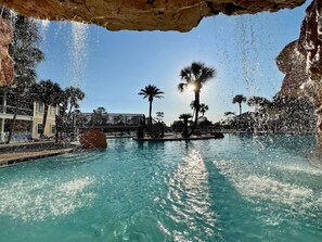 Un espace piscine avec une eau cristalline, des palmiers et une formation rocheuse.