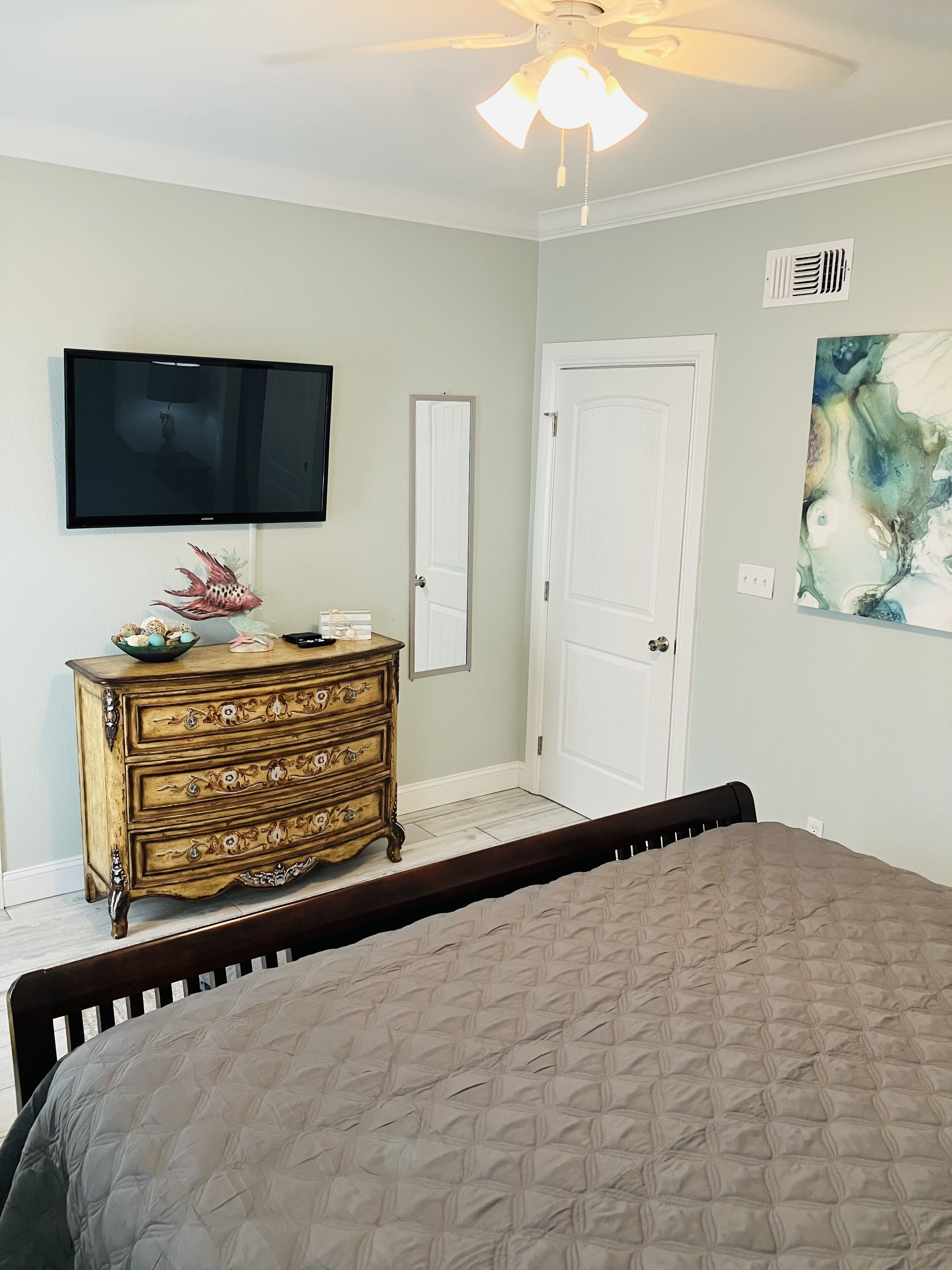 A bedroom with a bed, a dresser, a television mounted on the wall, and a door.