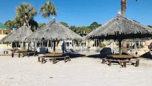 A beach with thatched umbrellas and wooden tables. - HangLoose14AD-Beautiful Beach Cottage@ the Purple Parrot Resort/Perdido Key FL (Pensacola)