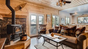 A cozy cabin interior with a wood-burning stove, a sofa with patterned cushions, and a dining table.